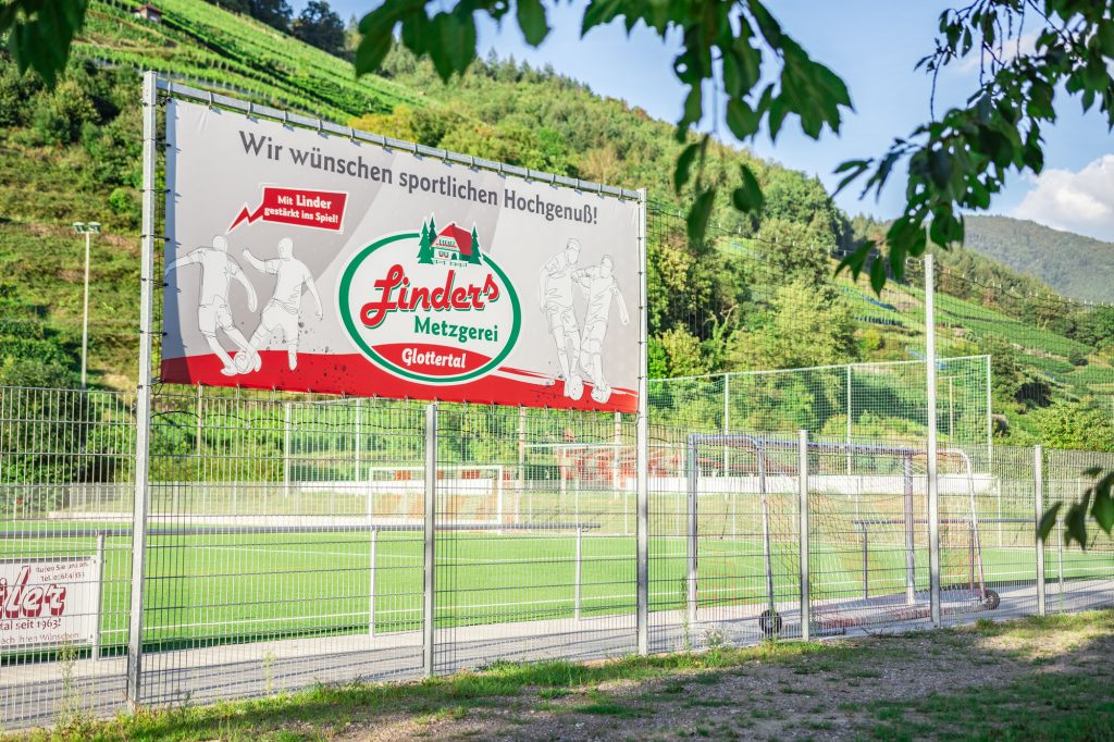 Gestaltung von Außenwerbung als Bannerwerbung wie ein Bauzaun an einem Fußballplatz mit Firmenlogo und Grafikdesign von der Werbeagentur STUDIO MÜLLER