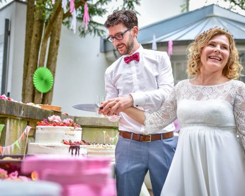 Baut und Bräutigam schneiden Ihre Hochzeitstorte bei Ihrer Hochzeit auf während Sie von Dennis Müller, dem Inhaber von STUDIO MÜLLER in Kenzingen fotografiert werden. Sie lachen und freuen sich über Ihre Hochzeit mit dem Hochzeitsfotograf in der Region